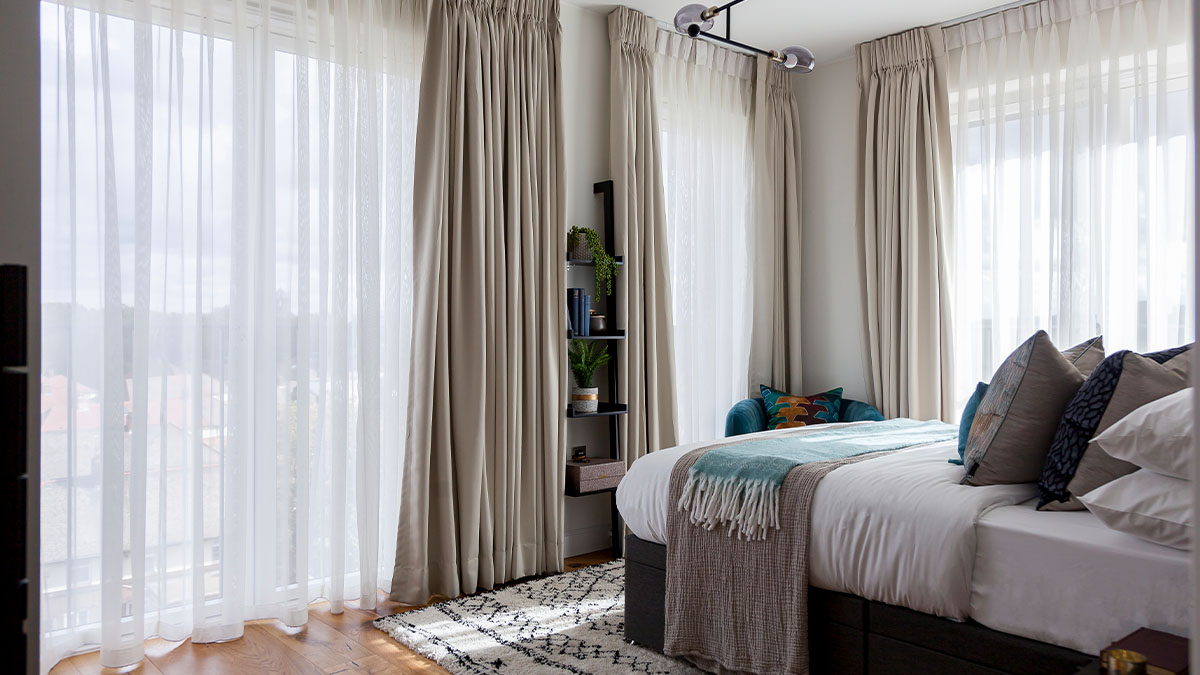 Bright bedroom with floor-to-ceiling curtains, cozy bed, and decorative pillows