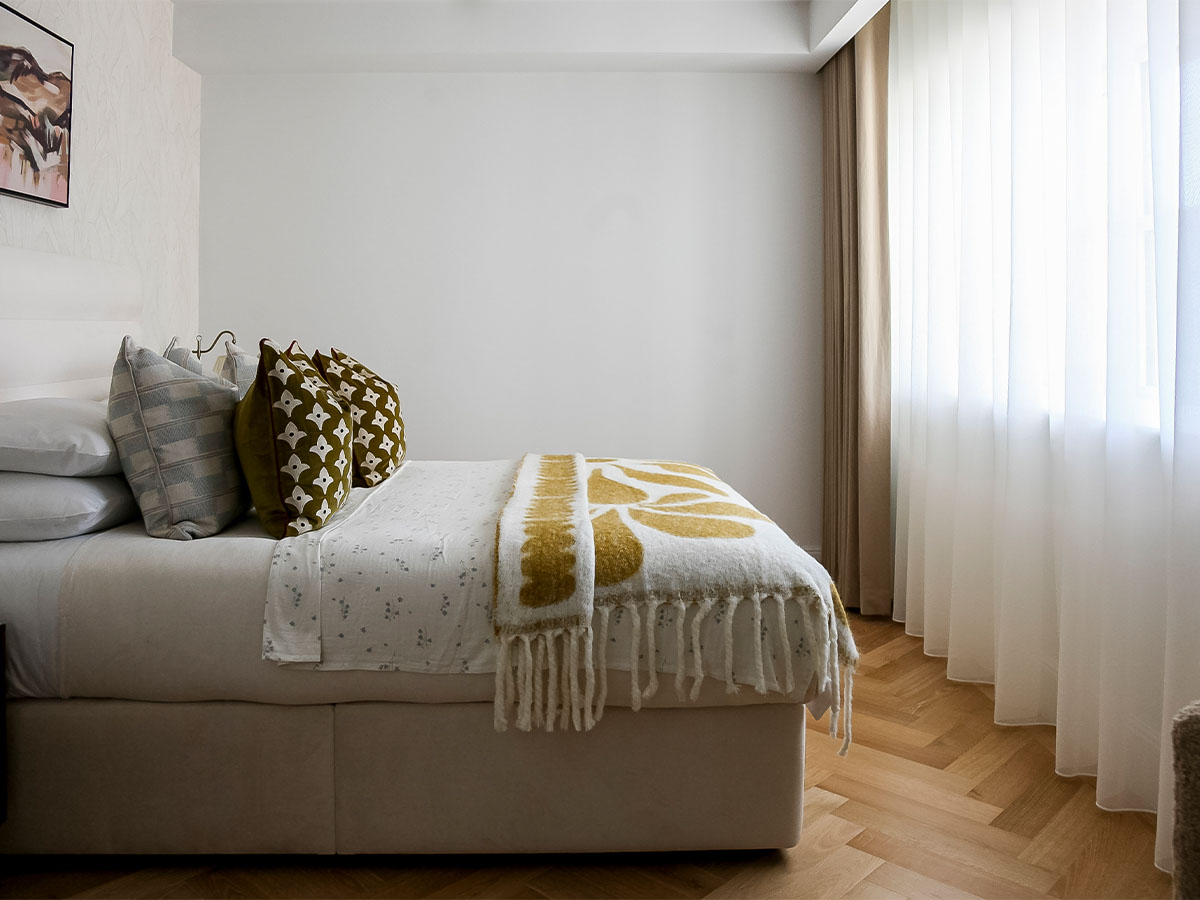 Modern bedroom with white bedding and yellow throw blanket of Milbank