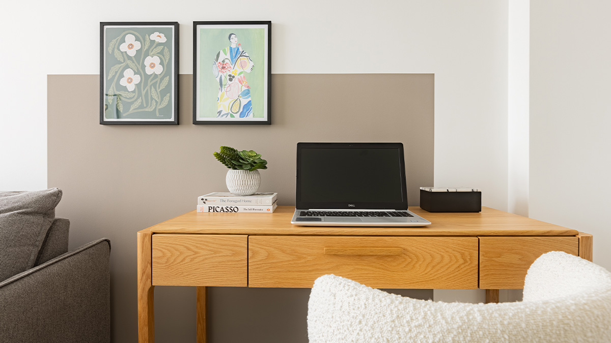 Modern home office with wooden desk, laptop, and artwork