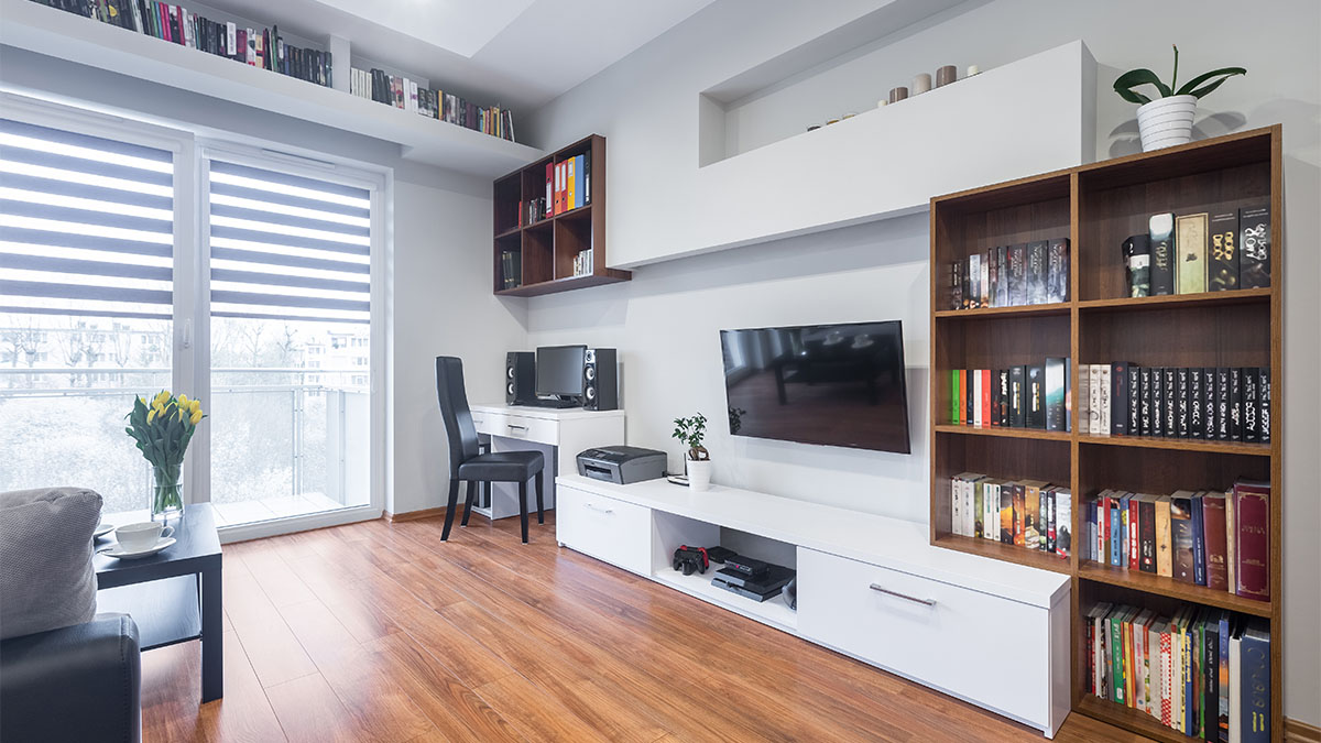 Modern entertainment room with wall-mounted TV, white media unit, wooden bookshelves, and hardwood flooring