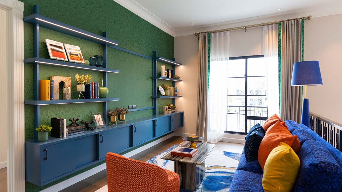 Modern living room featuring blue built-in shelving, green accent wall, navy sofa with colorful pillows, and coordinated decor elements